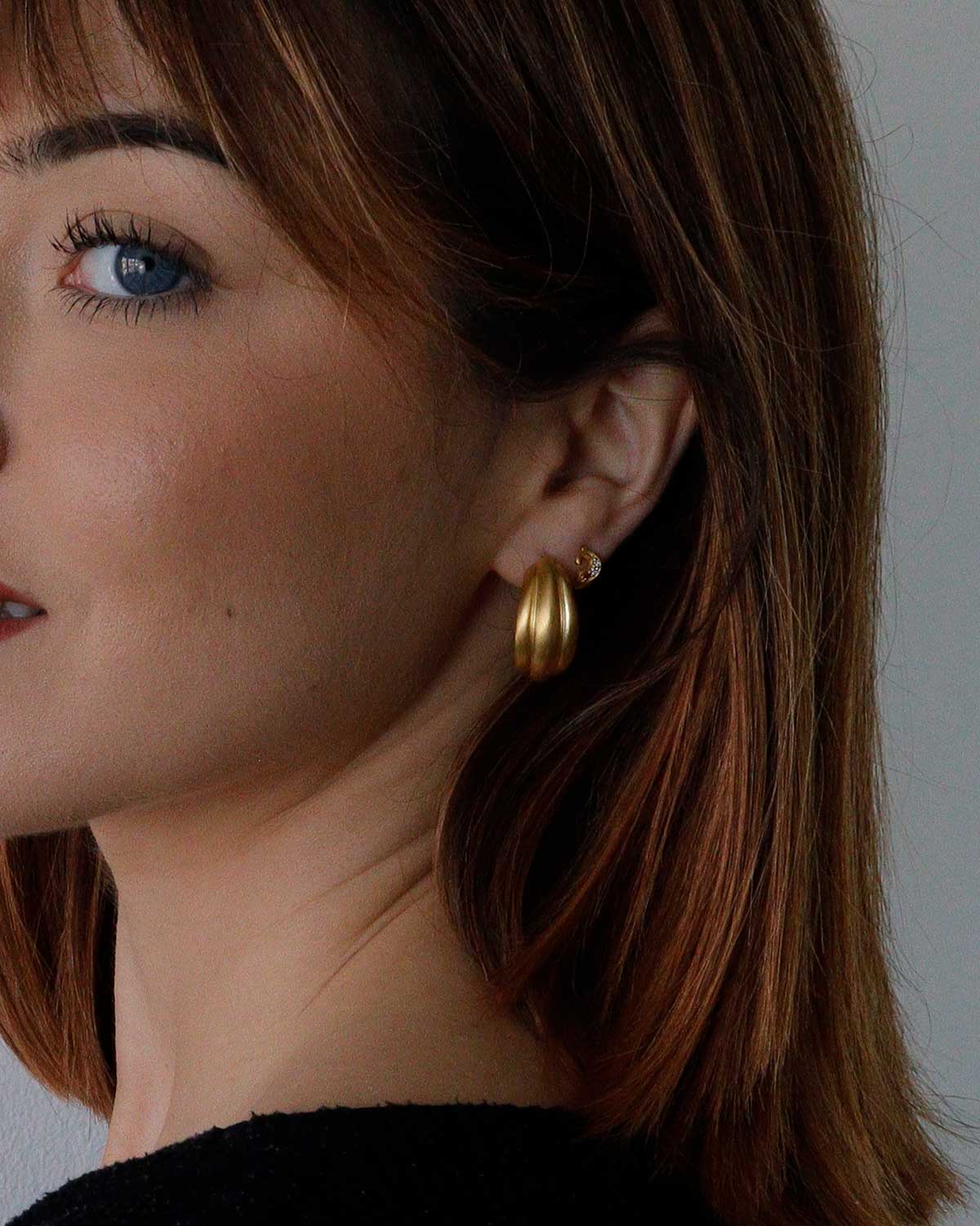 Close-up of chunky gold hoop earrings with brushed metal finish