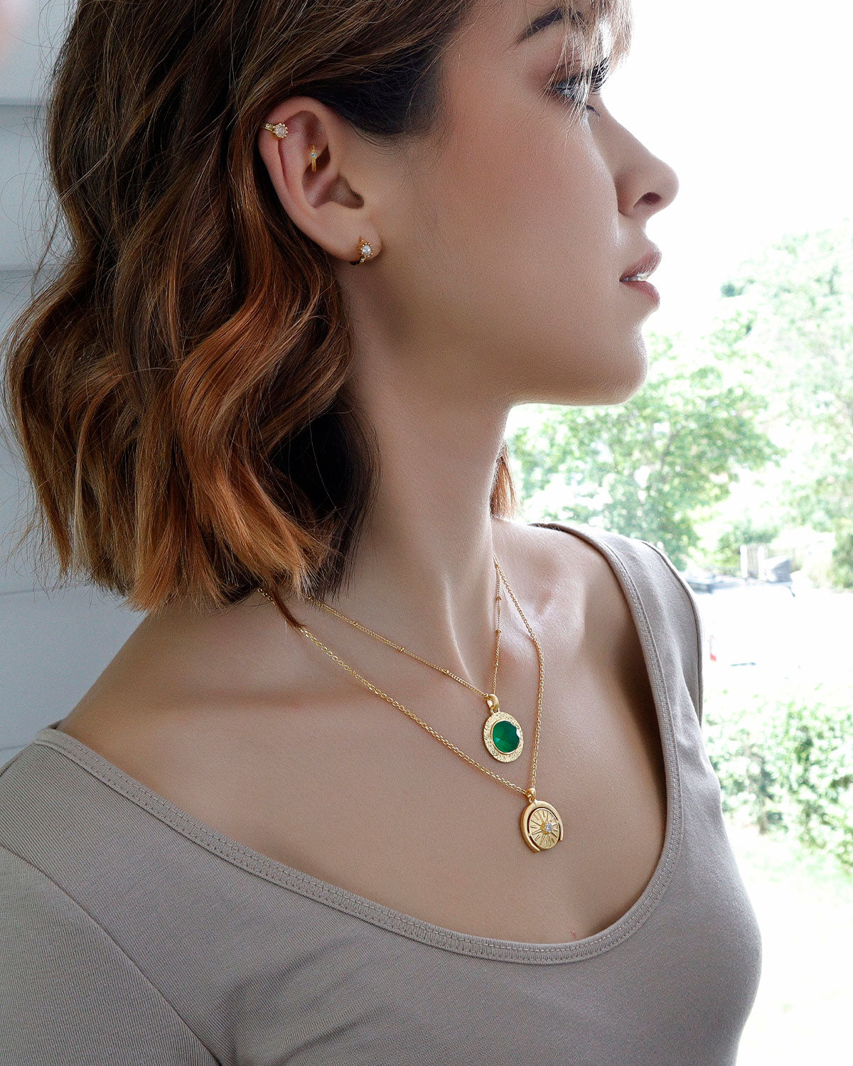 Model wearing gold necklace with circular green onyx gemstone