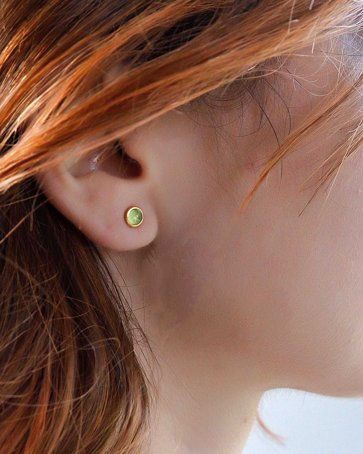 Model wearing peridot stud earrings with a subtle design