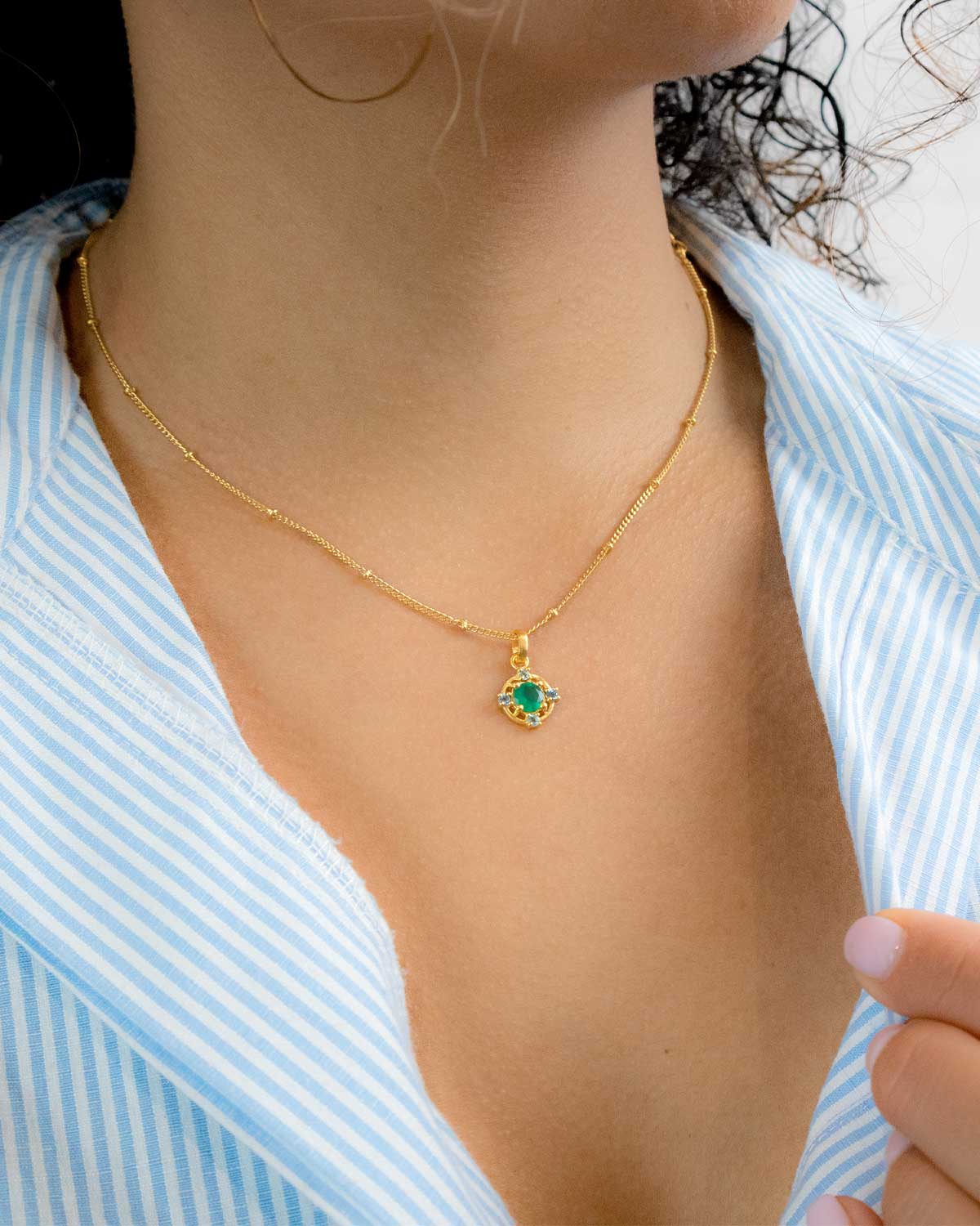 Model wearing gold necklace with green onyx and blue topaz gemstones