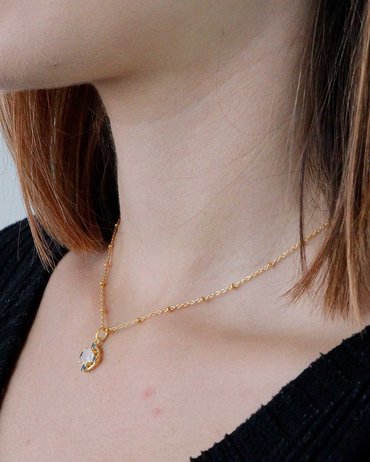 Model wearing gold necklace with moonstone and blue topaz gemstones