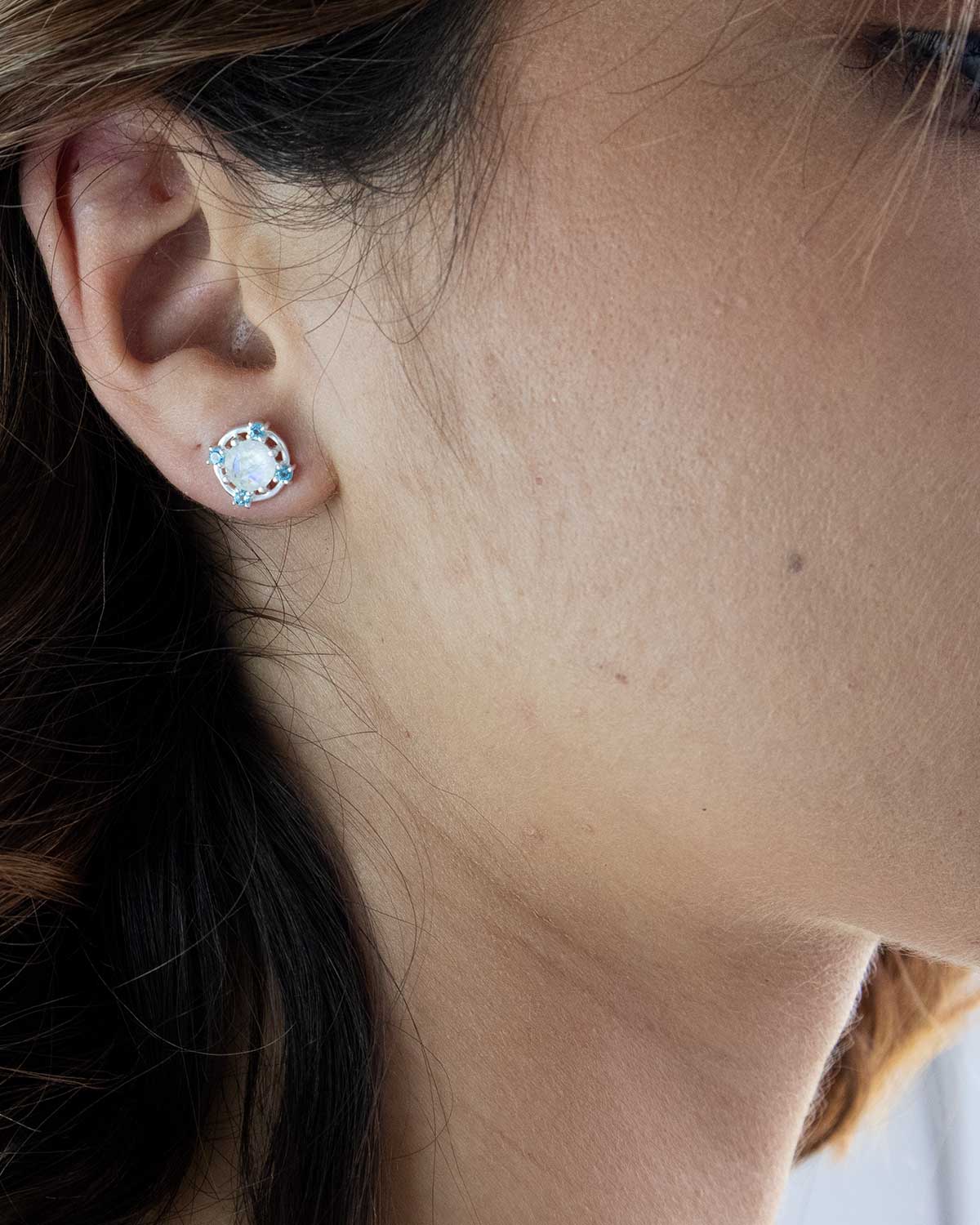 Model wearing silver stud earrings with moonstone and blue topaz gemstones