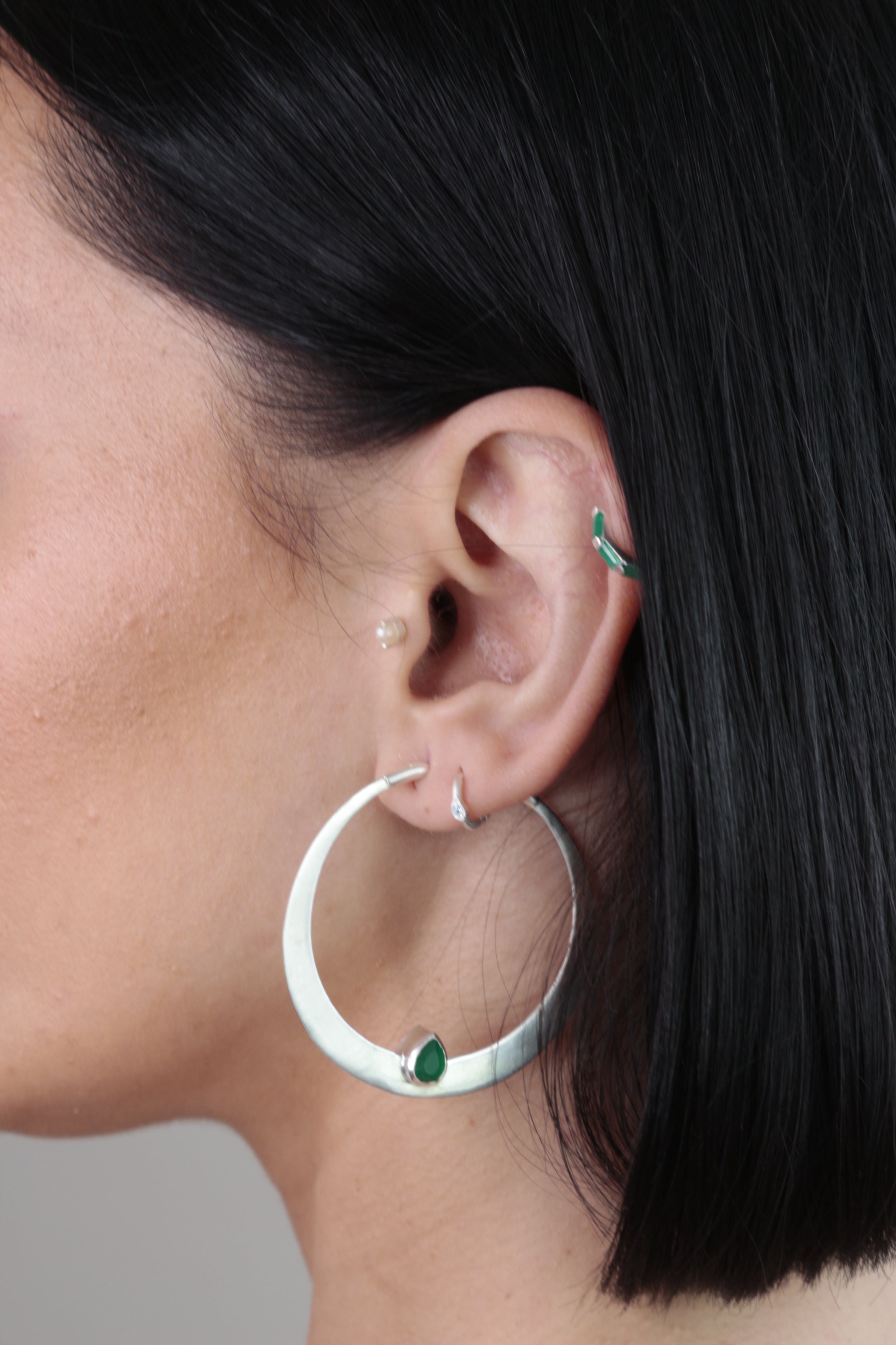 Model wearing large silver hoop earrings with green onyx gemstones