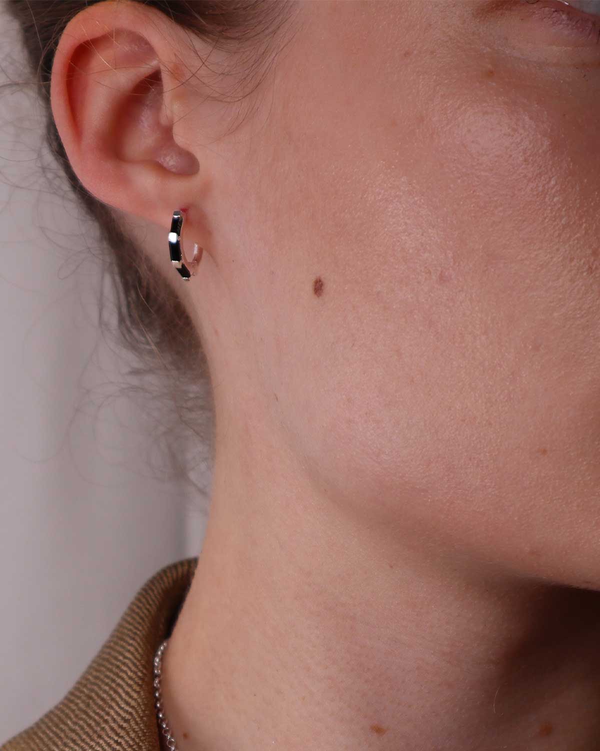 Close-up of silver mini hoops featuring baguette-cut black spinel gemstones