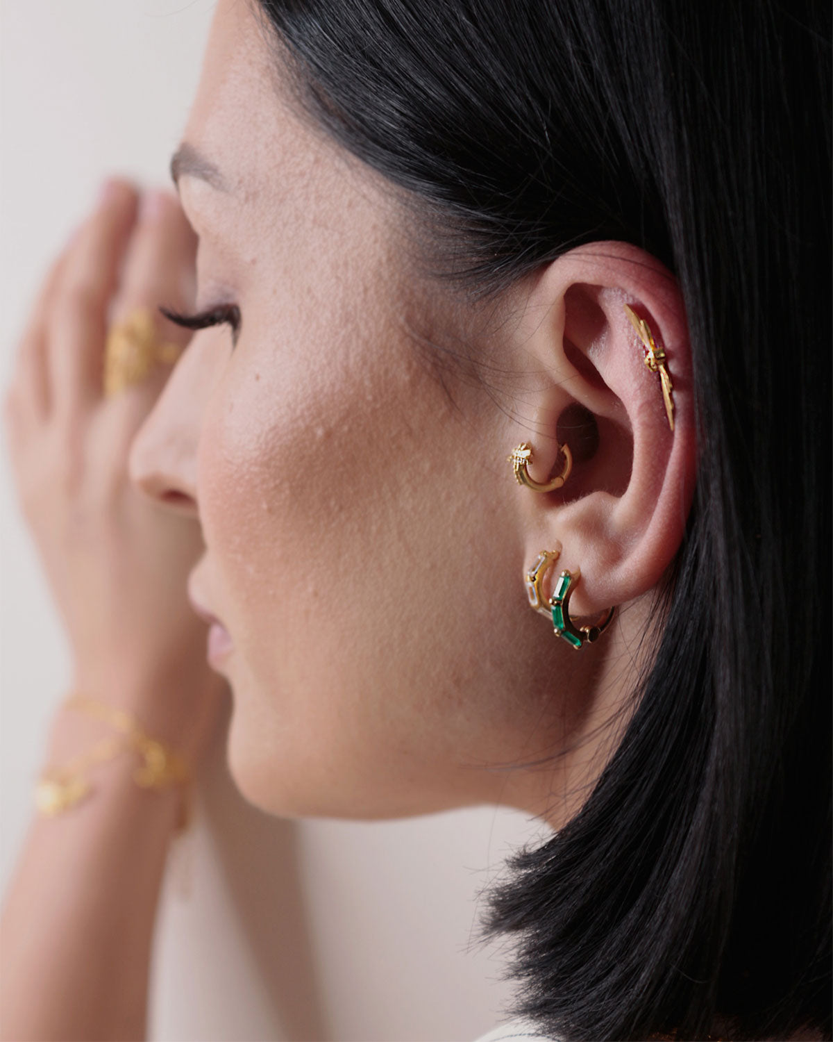 Close-up of gold mini hoop earrings with emerald green onyx gemstones