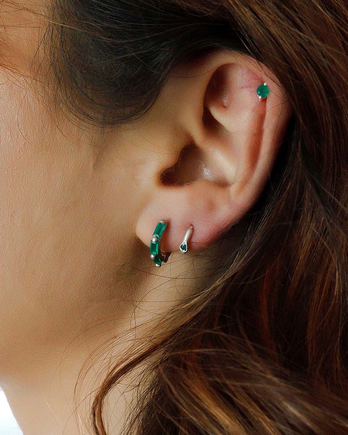 Close-up of silver mini hoop earrings with emerald green baguette-cut gemstones