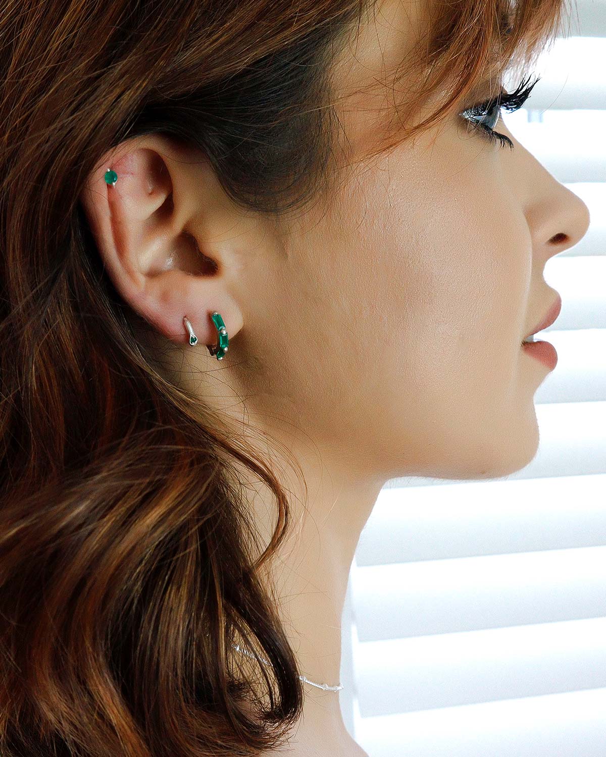 Model wearing silver mini hoop earrings with emerald green onyx gemstones