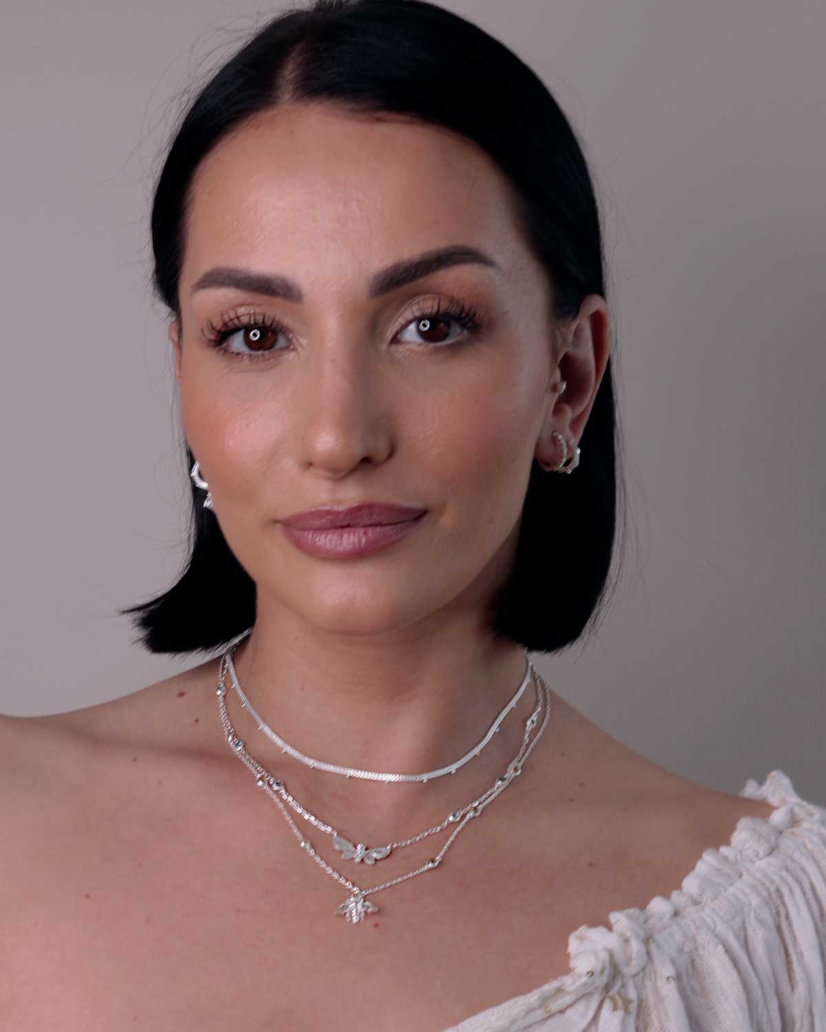 Silver butterfly necklace layered with other jewelry, highlighting blue topaz and pink tourmaline gemstones