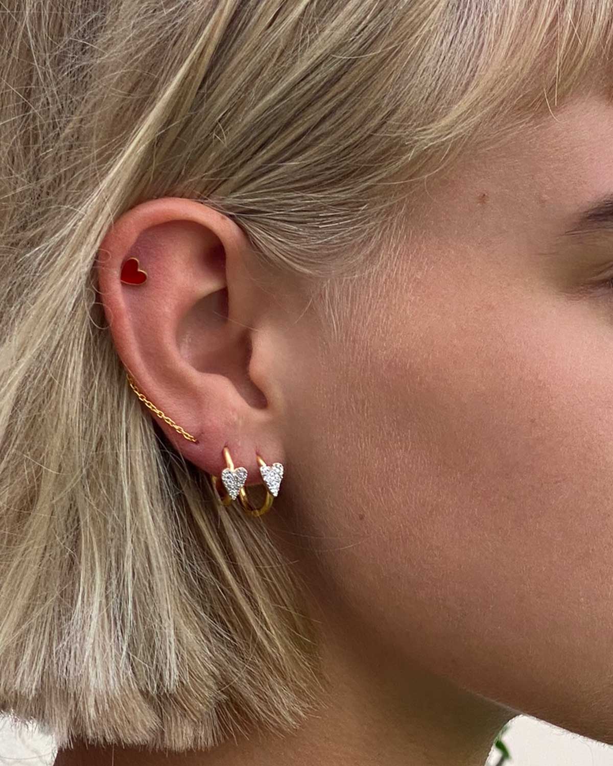 Model wearing gold earrings with red enamel heart charms