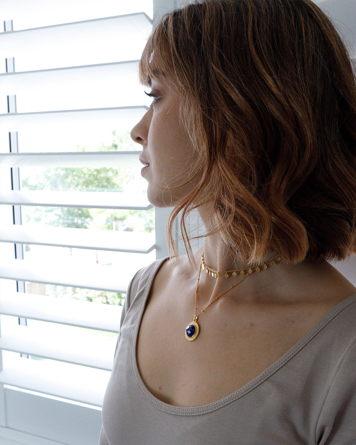 Model wearing gold necklace with circular lapis lazuli pendant