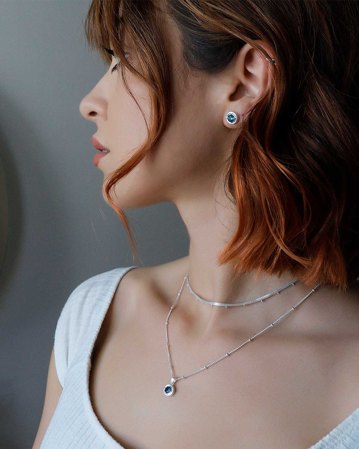 Model wearing sterling silver stud earrings with blue topaz gemstones