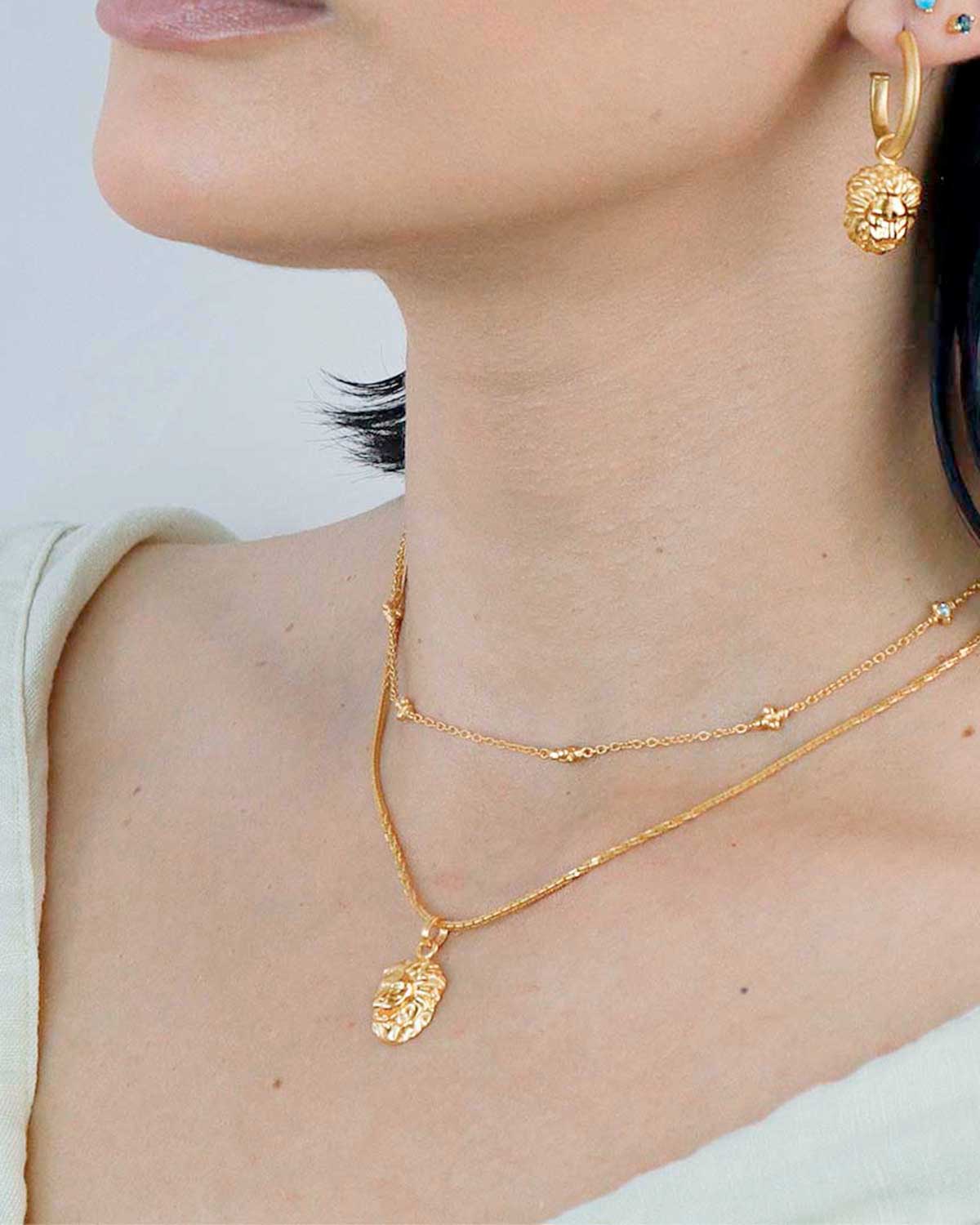 Model wearing a gold lion pendant necklace with a textured chain