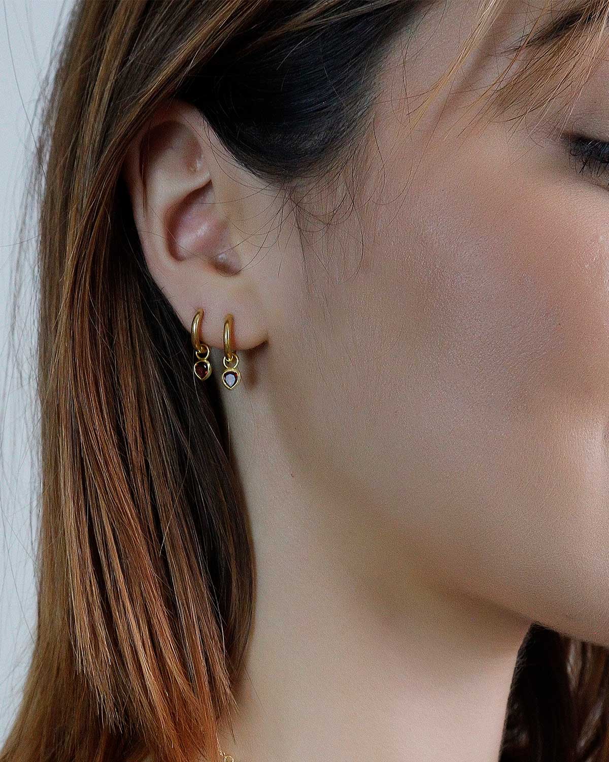 Model wearing gold mini hoop earrings with garnet heart charms