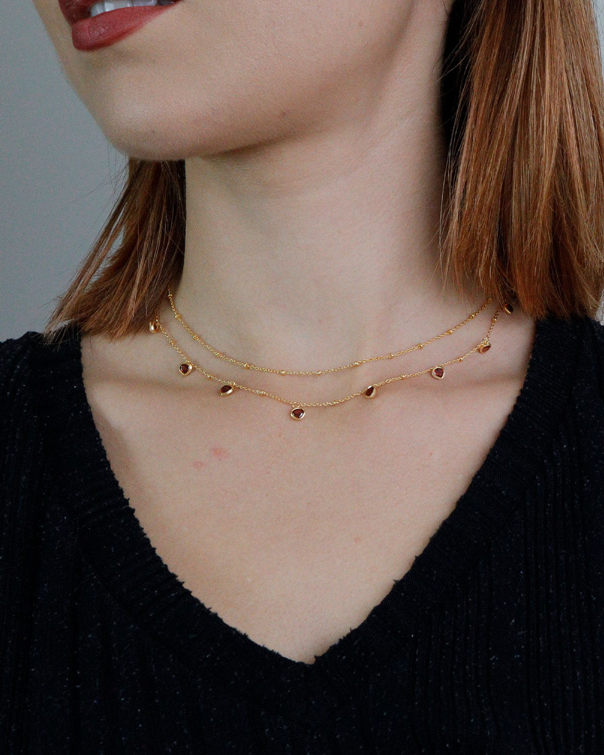 Model wearing a gold necklace with a garnet heart charm