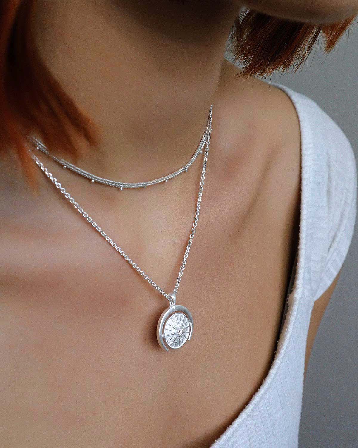 Model wearing sterling silver necklace with a circular diamond pendant