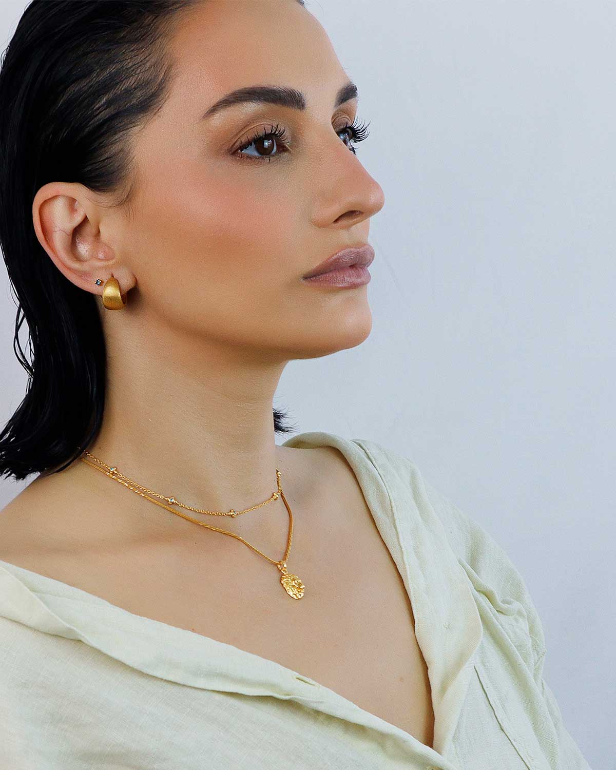 Side view of chunky gold mini hoop earrings with a polished satin finish