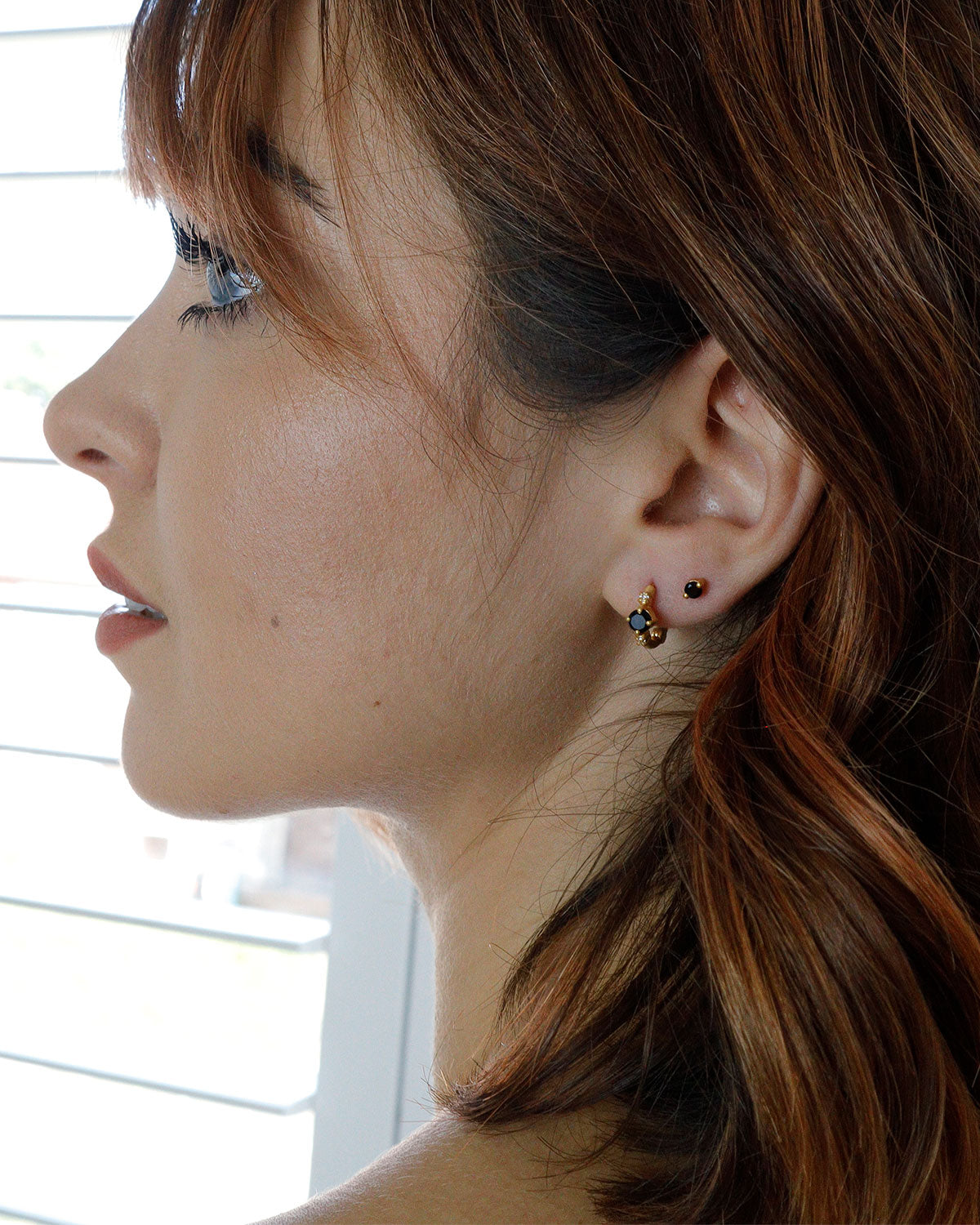 Model wearing gold mini hoop earrings with black spinel and pearls
