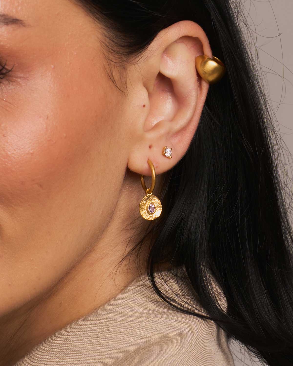 Close-up of a person wearing gold hoop earrings with pink gemstones.