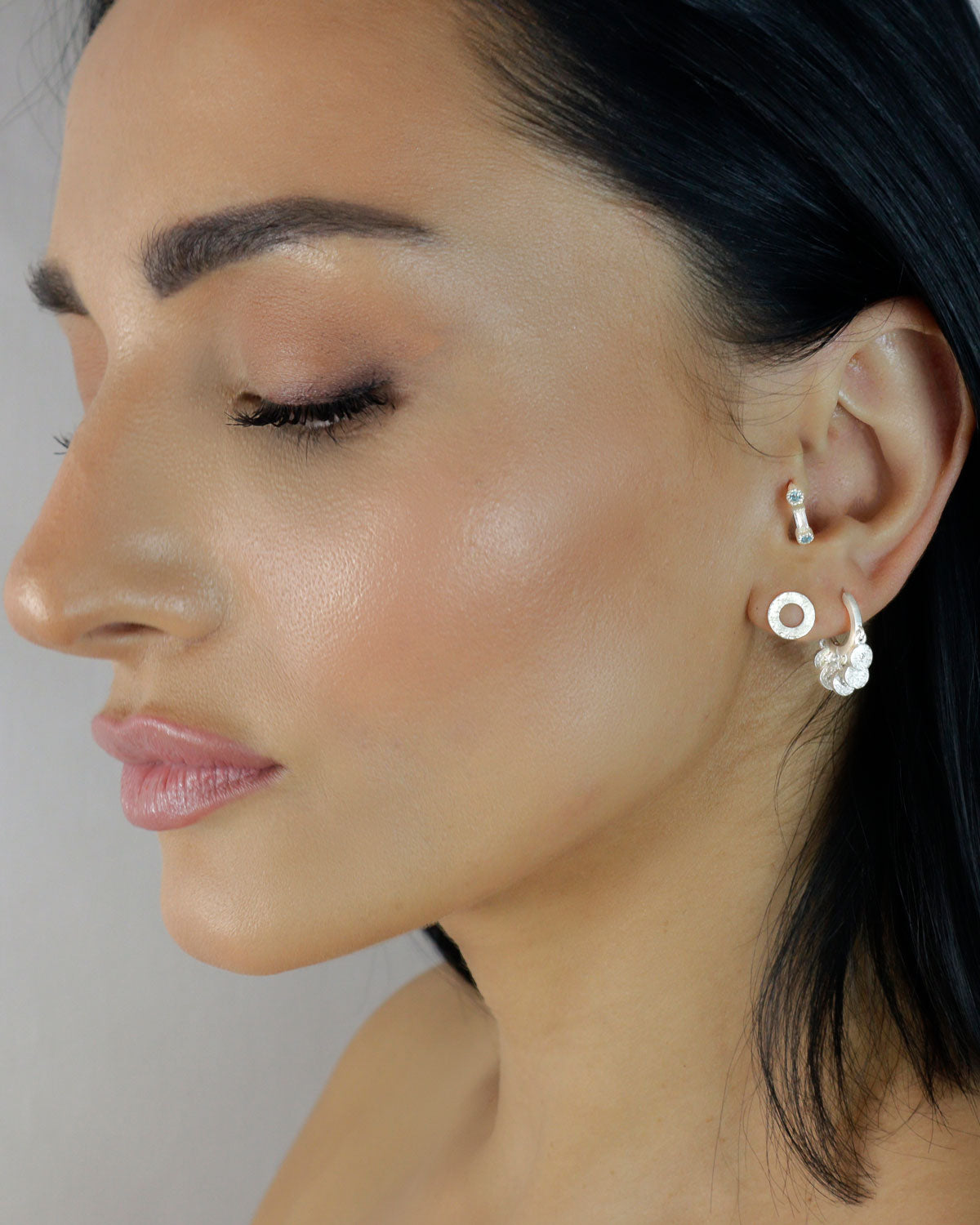 Close-up of silver mini hoops with crystal charms and textured surface