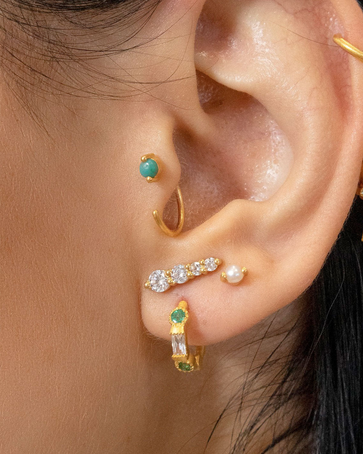 Gold mini hoop earrings styled in a stacked look with emerald gemstones