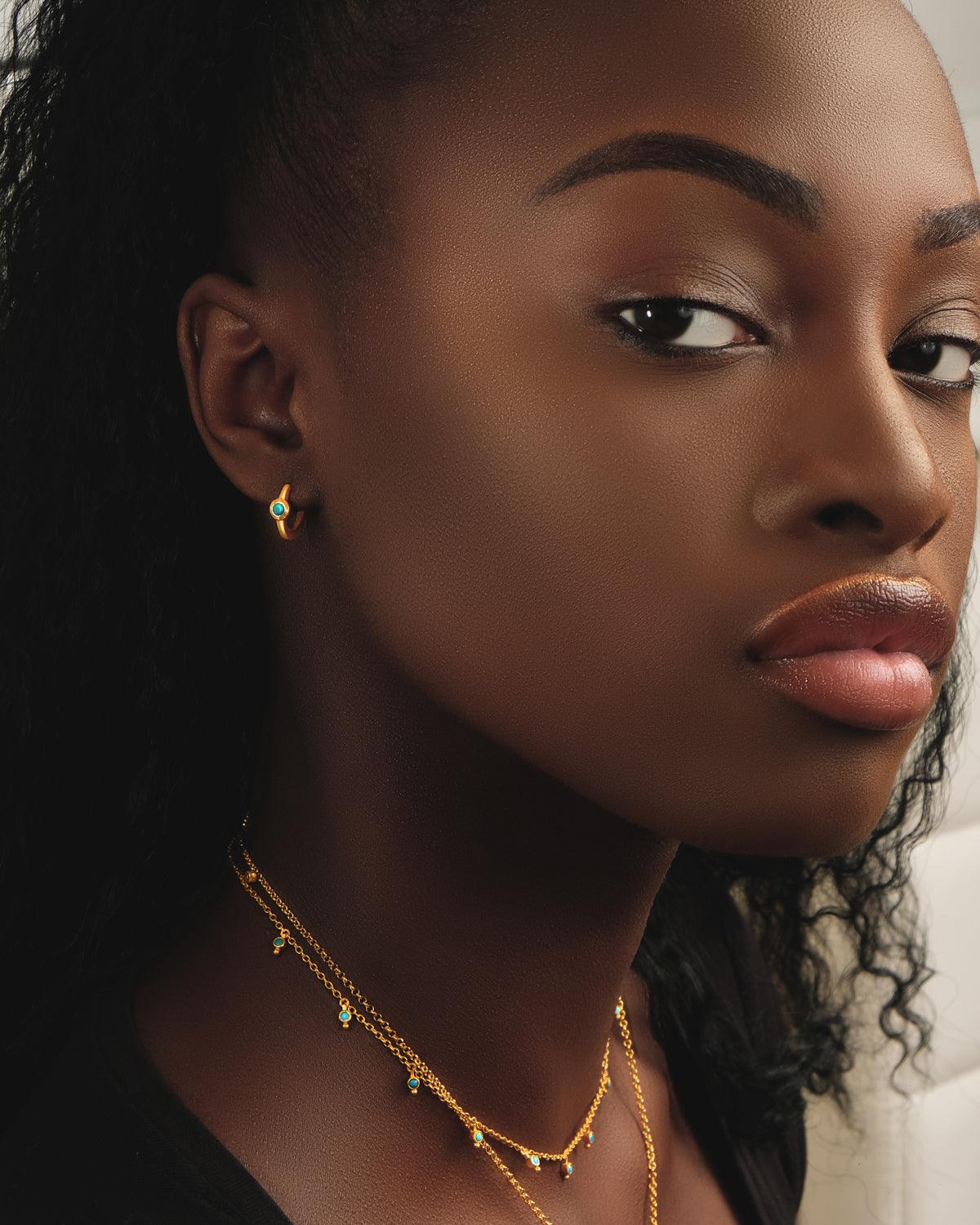 Close-up of gold huggie earrings with hand-cut turquoise gemstones