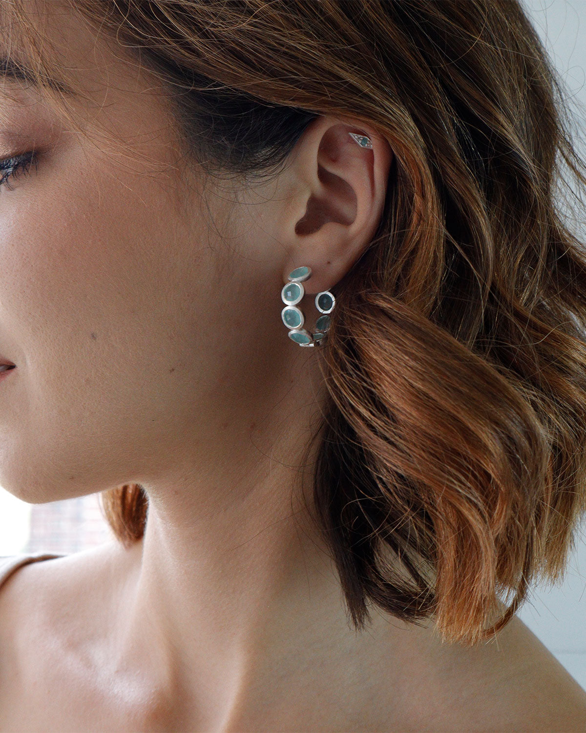 Close-up of silver hoop earrings with aqua gemstones