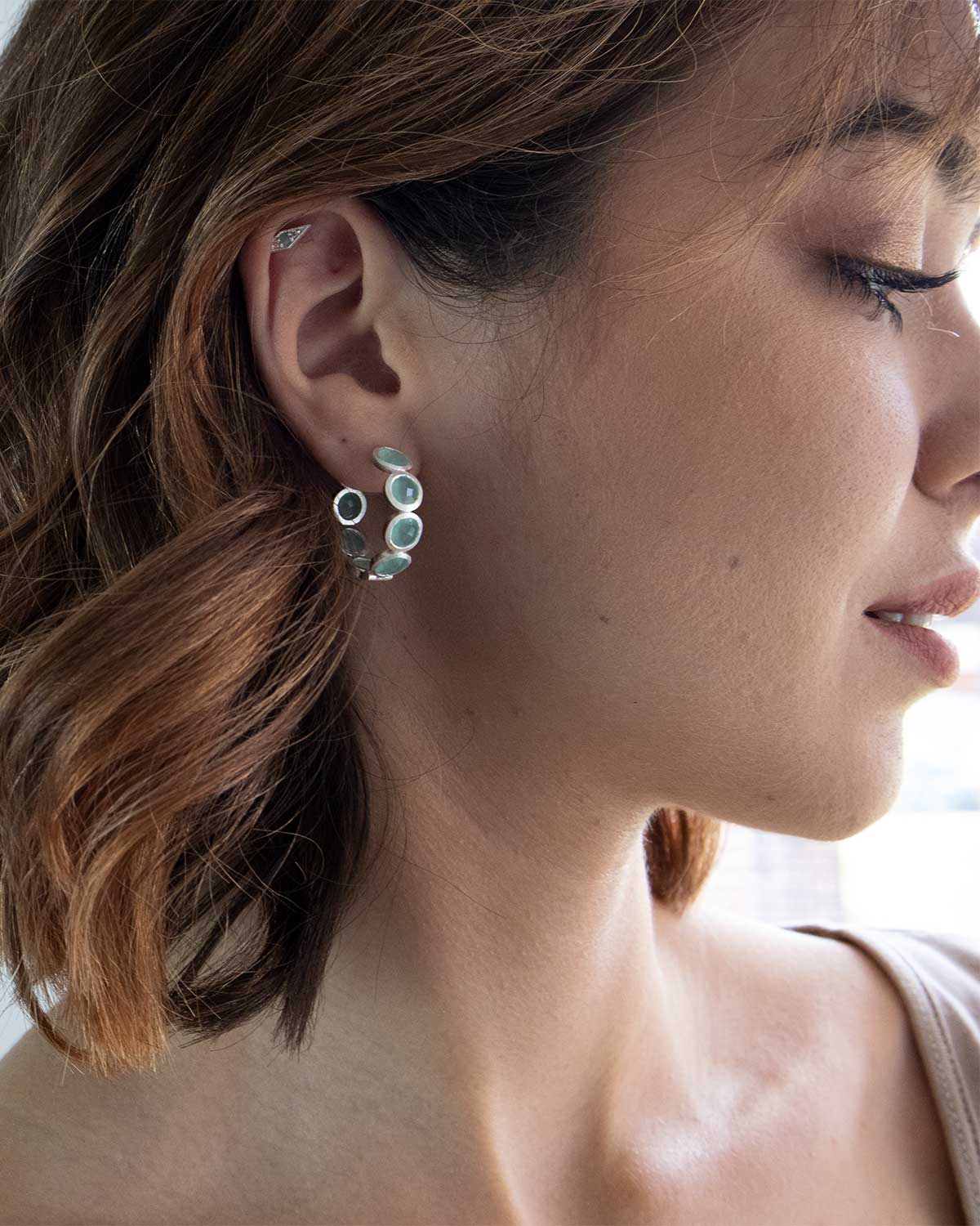 Model wearing small silver hoop earrings with aqua gemstones