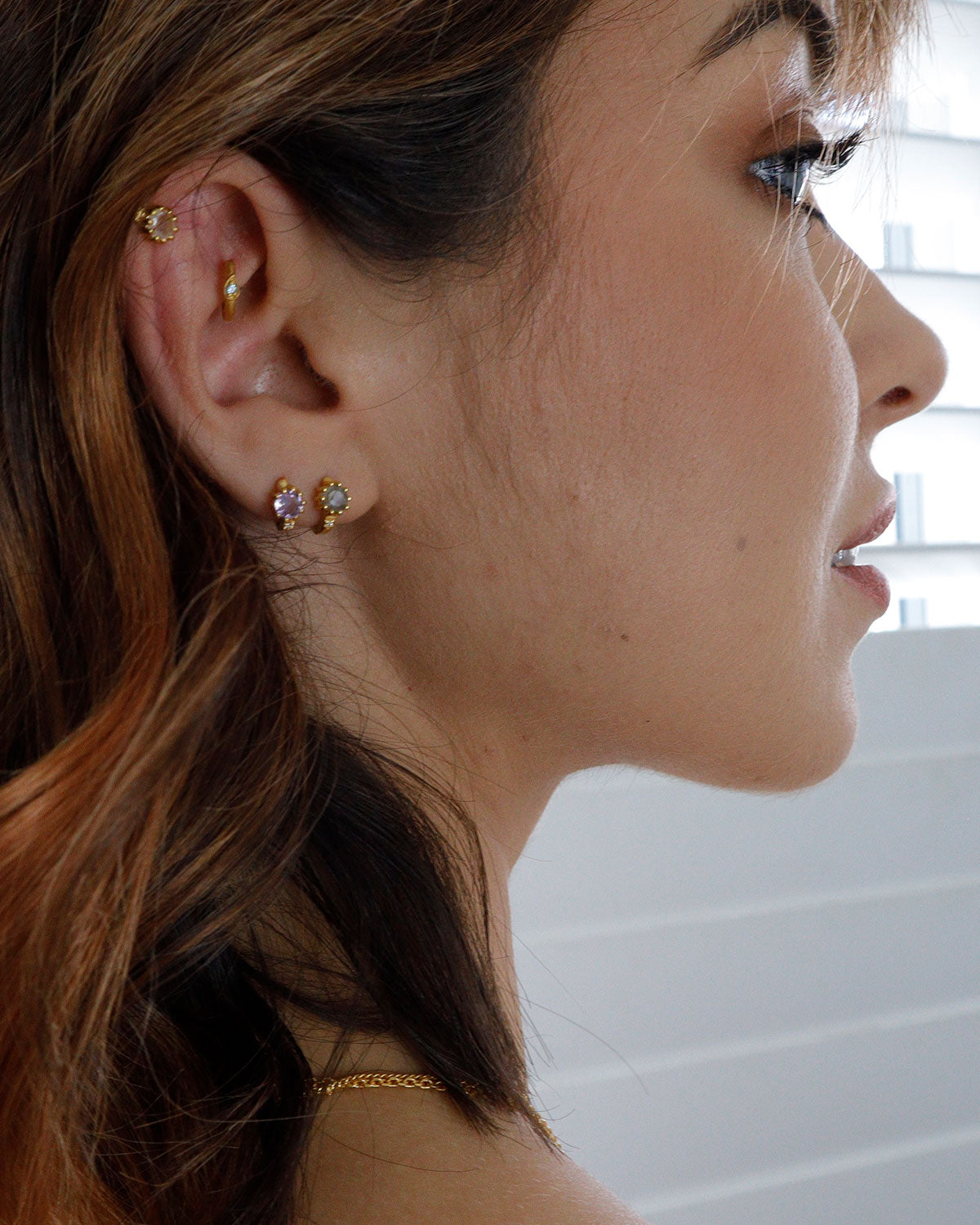 Close-up of silver huggie earrings with mixed gemstones and matte finish