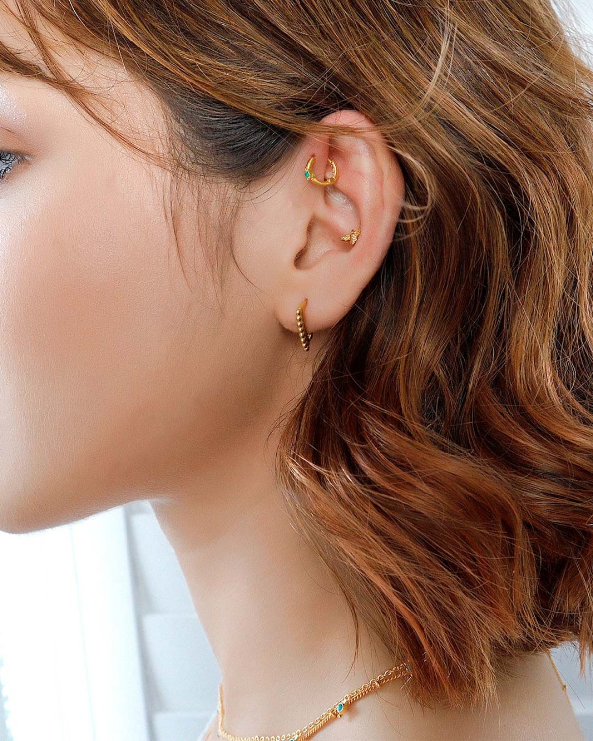 Model wearing mini gold bee stud earrings in multiple ear piercings