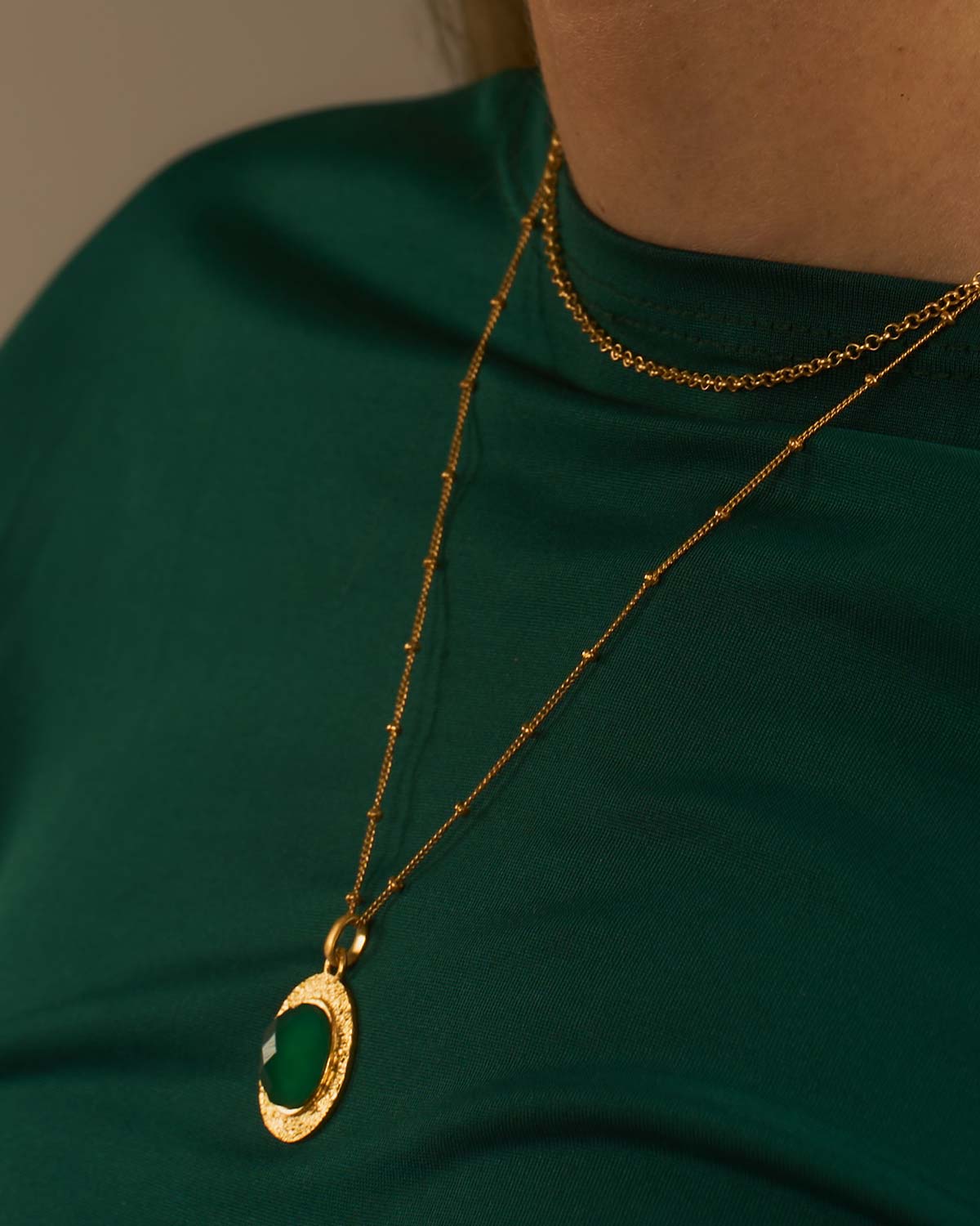 Detailed view of circular green onyx gemstone set in a gold necklace