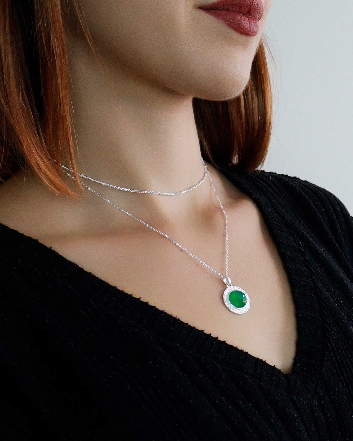 Model wearing silver necklace with circular green onyx pendant
