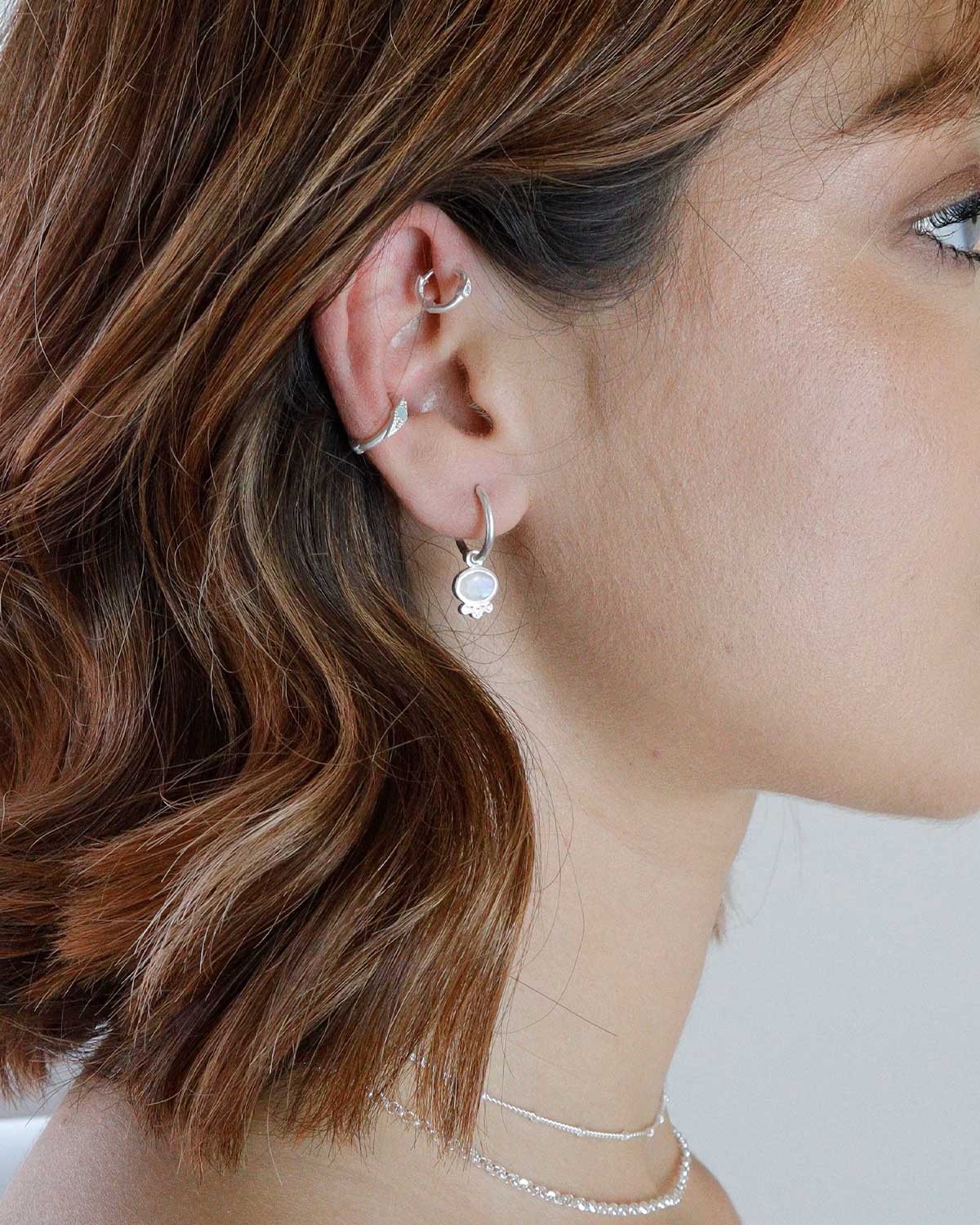 Close-up of silver mini hoops with hand-cut rainbow moonstone charm