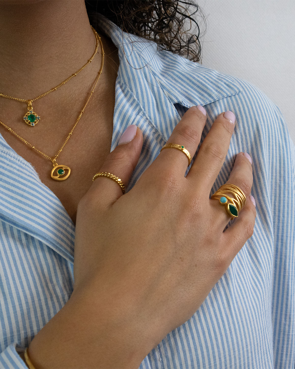 Model wearing gold rings with green onyx and turquoise gemstones