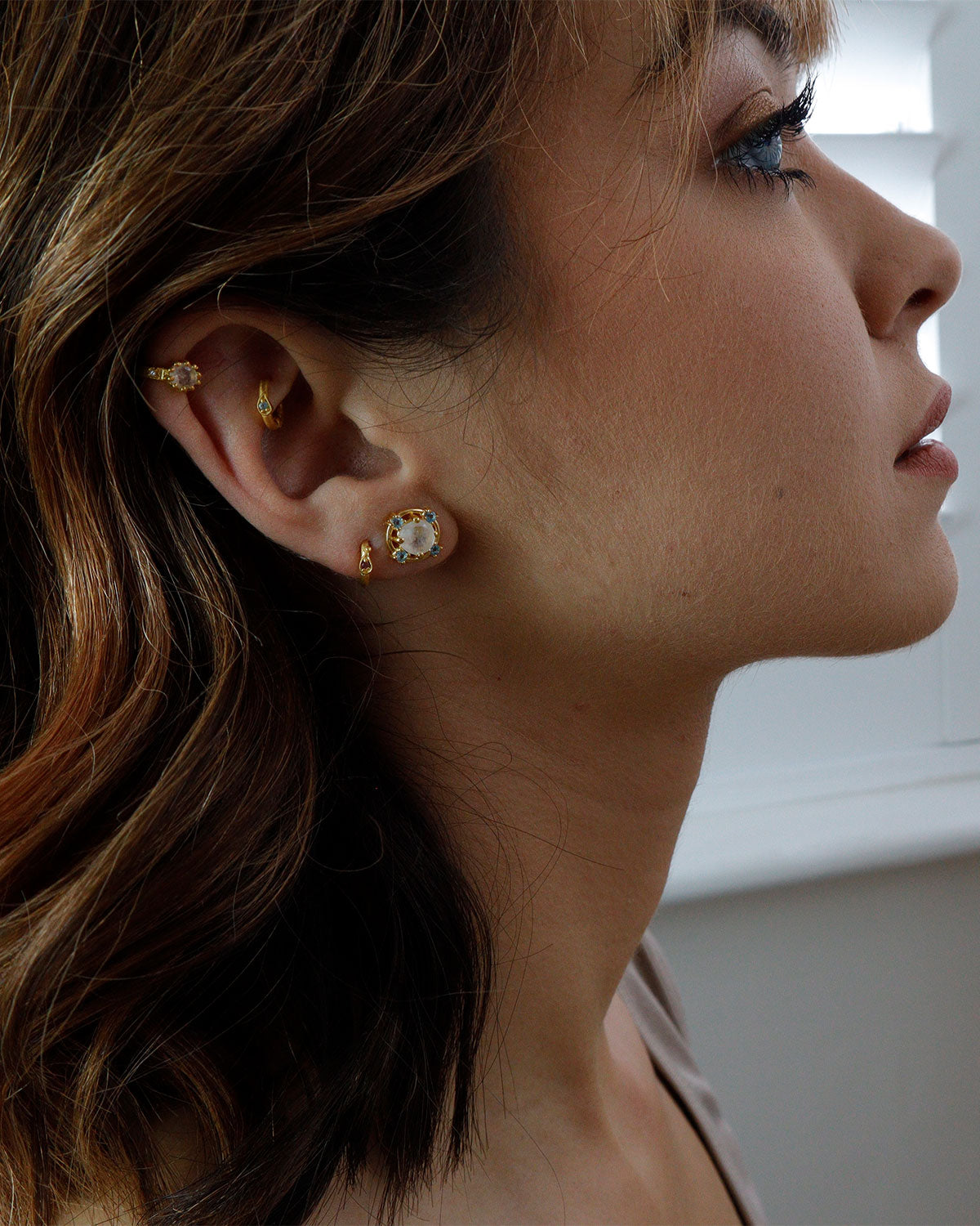 Model wearing gold stud earrings with moonstone and blue topaz