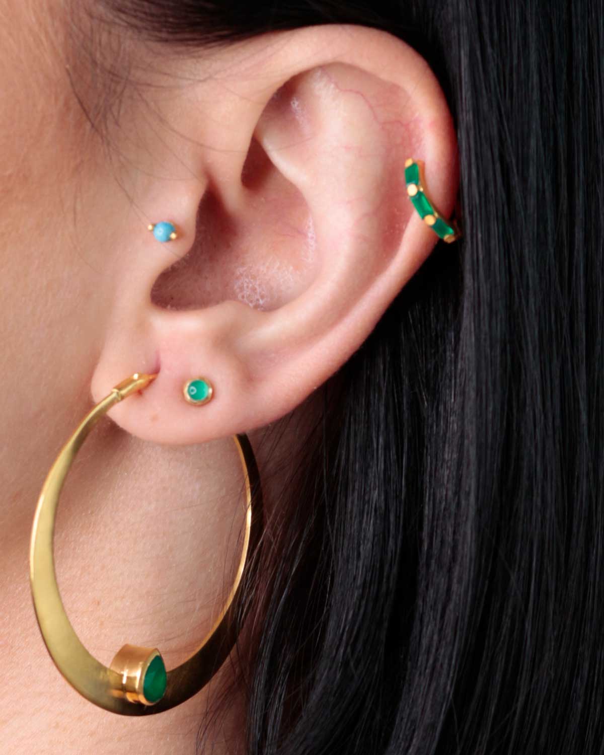 Gold mini hoop earrings with emerald green gemstones styled with other earrings