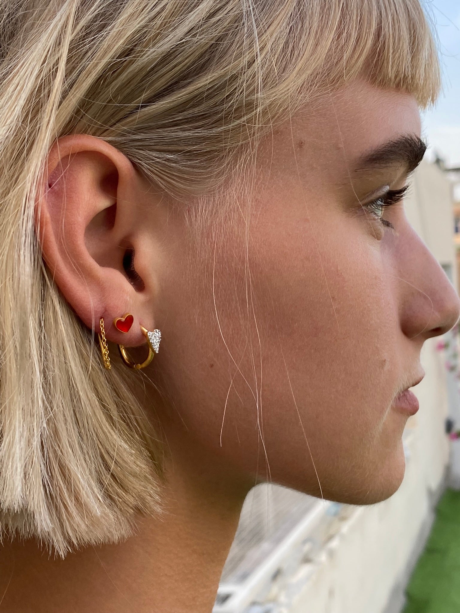 Close-up of silver earrings with lipstick red enamel heart detail