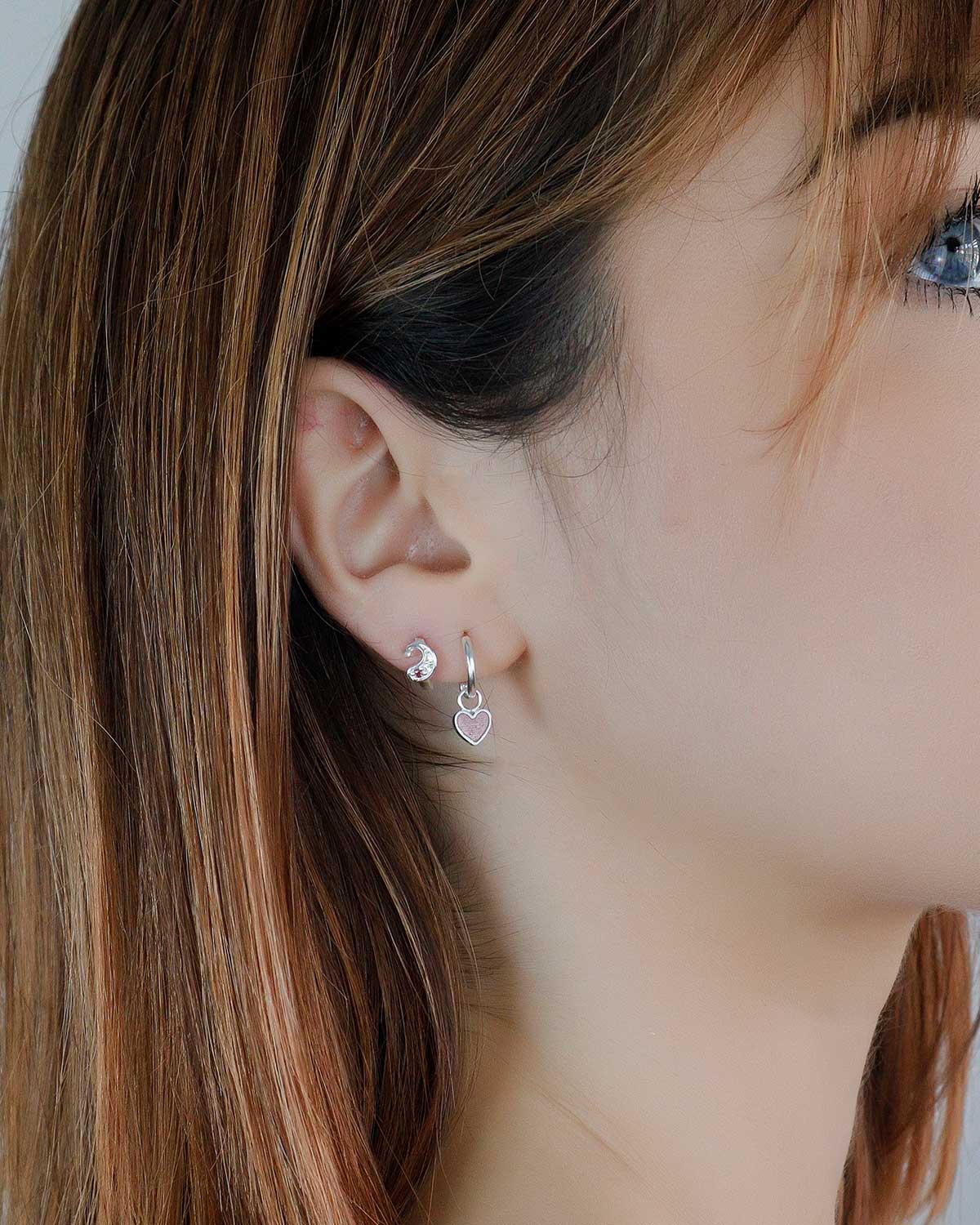 Model wearing silver mini hoop earrings with lipstick-coloured enamel heart charms