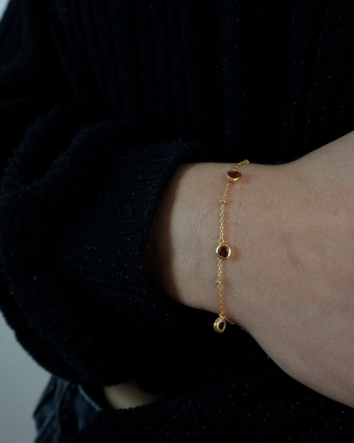 Model wearing a gold bracelet with a garnet heart charm