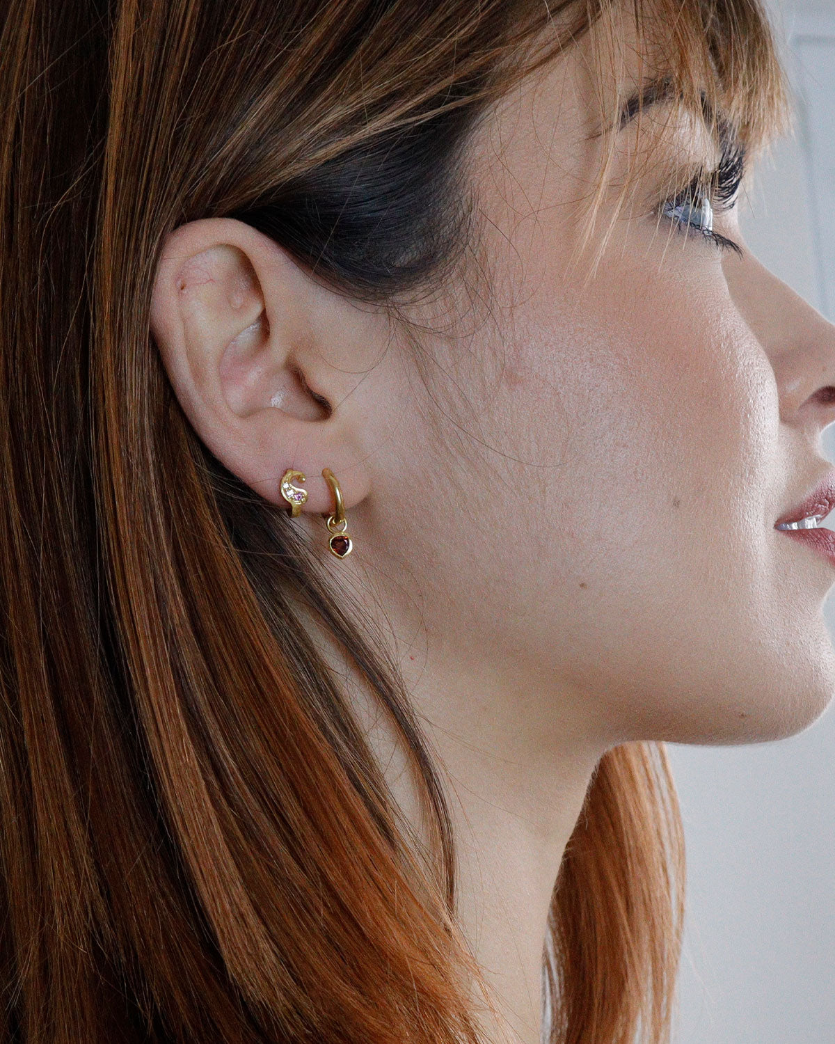 Close-up of garnet heart charms on gold mini hoop earrings