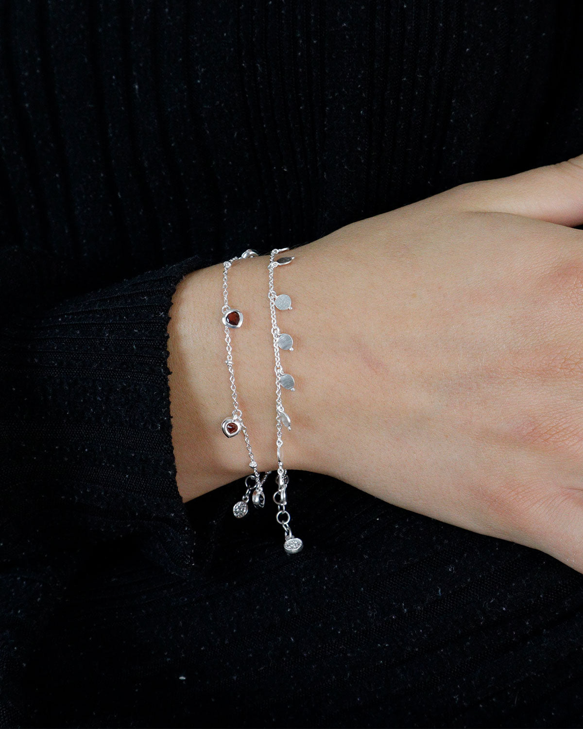 Sterling silver bracelet with a garnet heart charm worn on the wrist