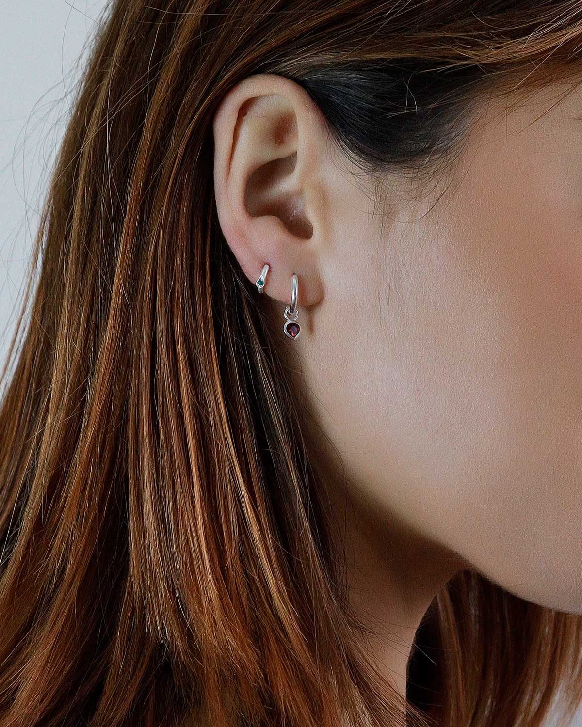 Close-up of silver mini hoop earrings with garnet heart charm details