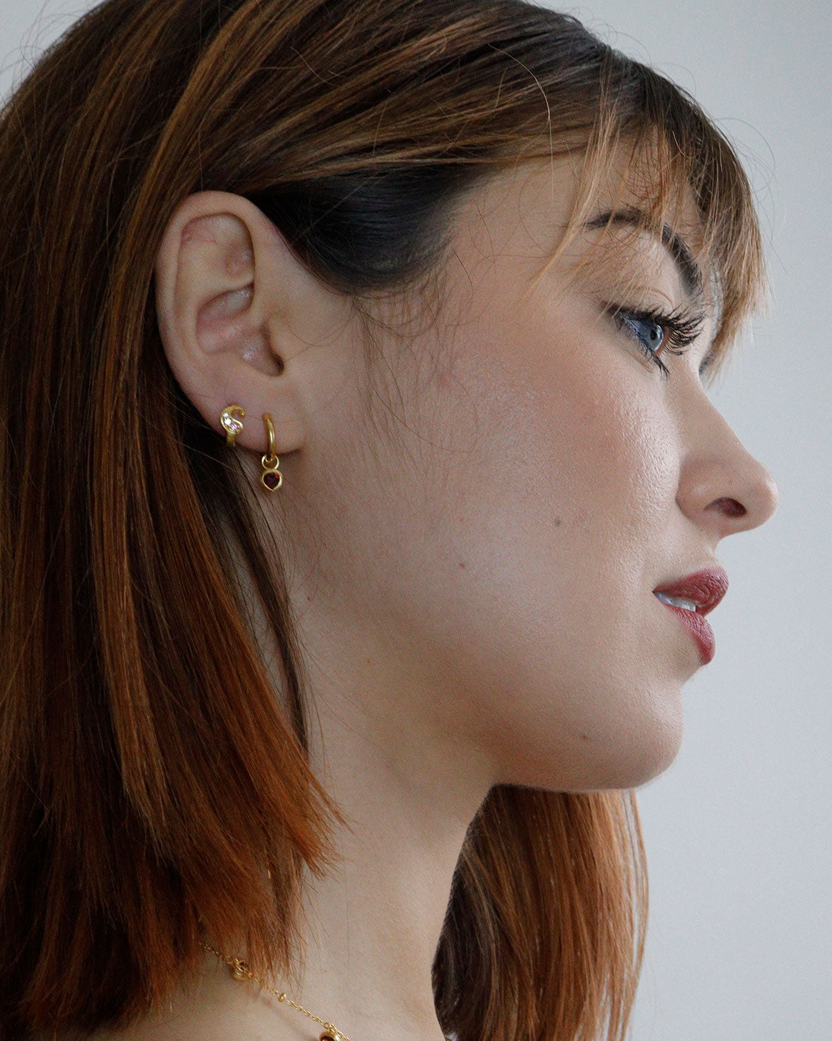 Model wearing silver mini hoop earrings with garnet heart charms
