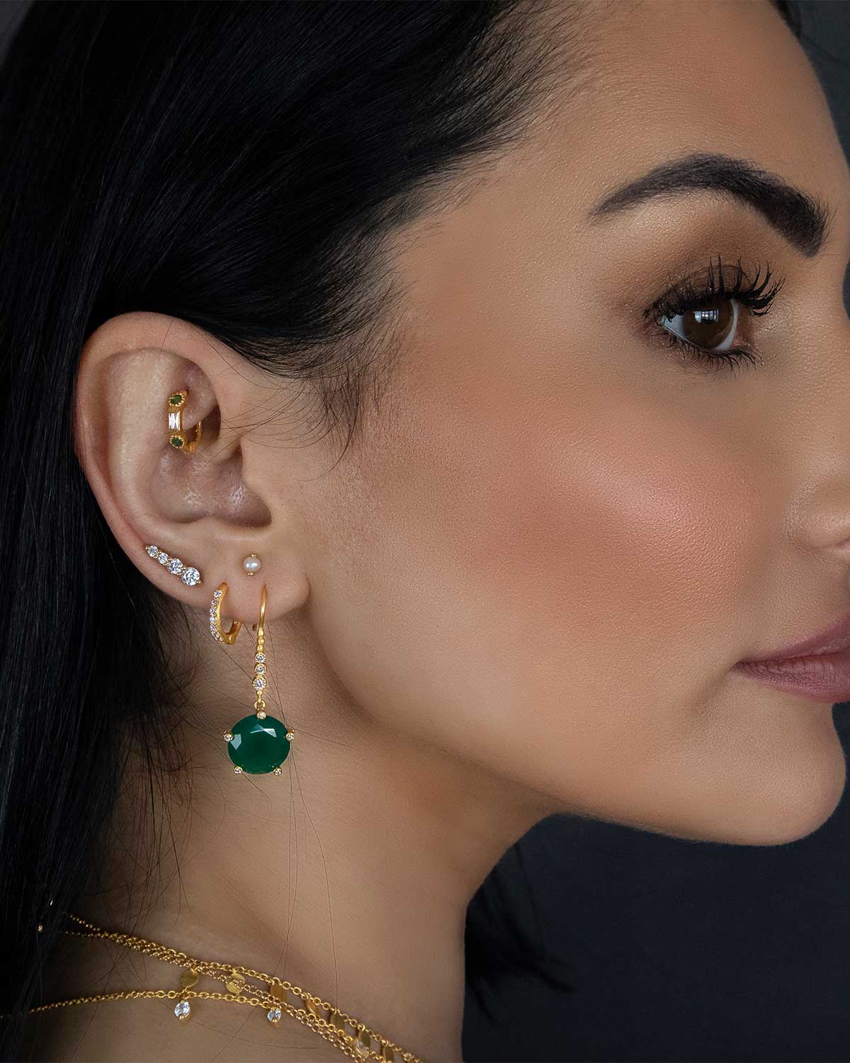 Silver mini hoop earrings with emerald stones styled in a stacked look