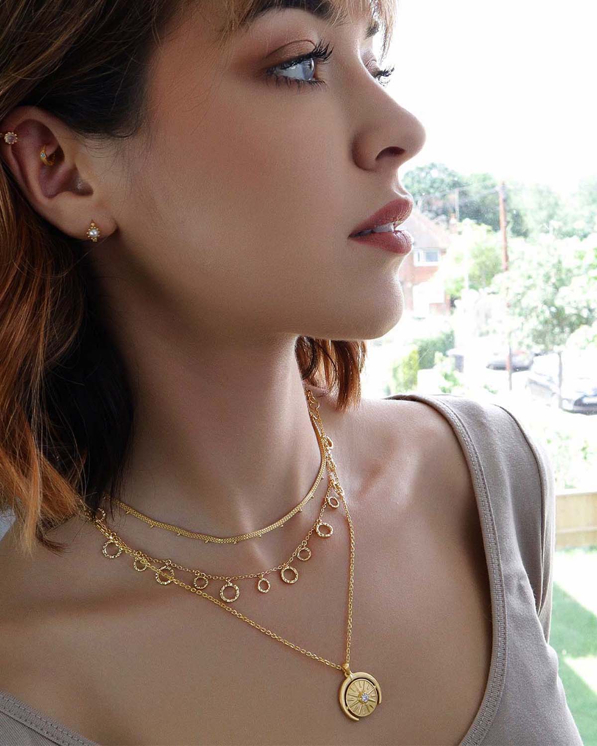 Gold pendant necklace styled in a layered look with other chains