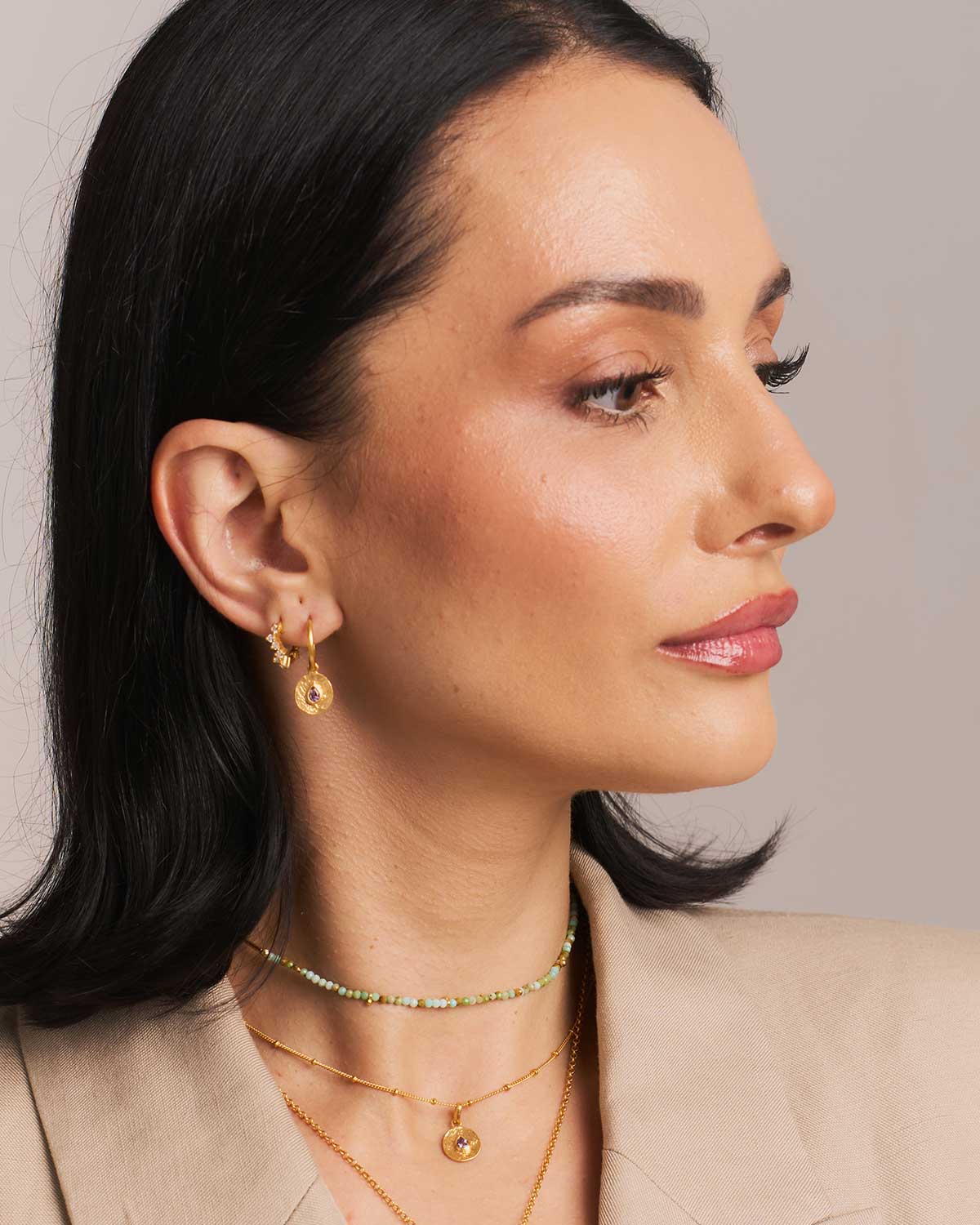 A woman wearing gold earrings with a removable dainty disk set with pink amethyst