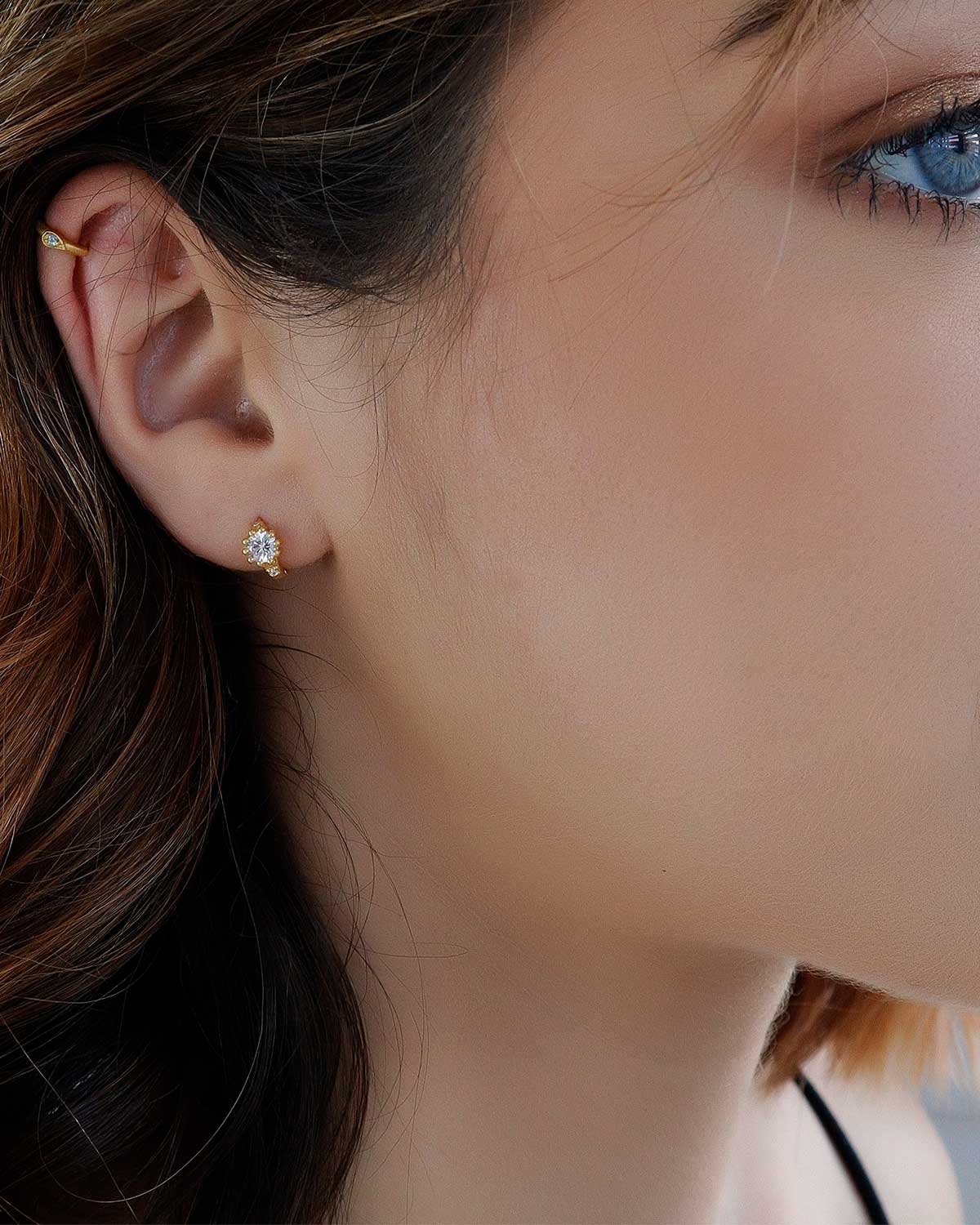 Gold huggie earrings styled in a stacked look with multiple gemstones