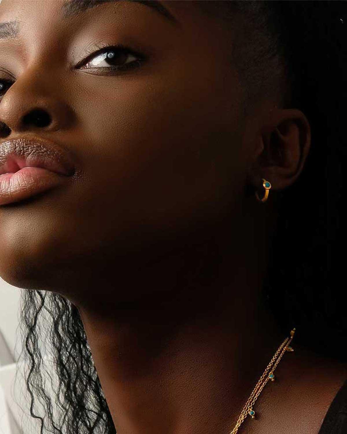 Model wearing gold huggie earrings with turquoise gemstones