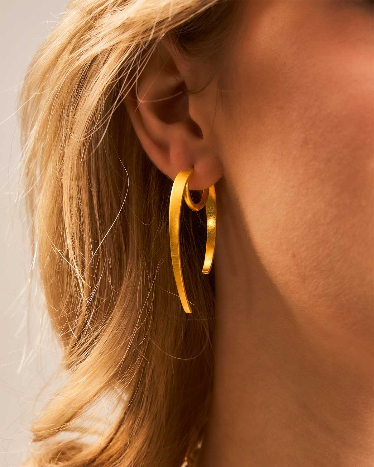 Gold hoop earring worn by a model with blonde hair.