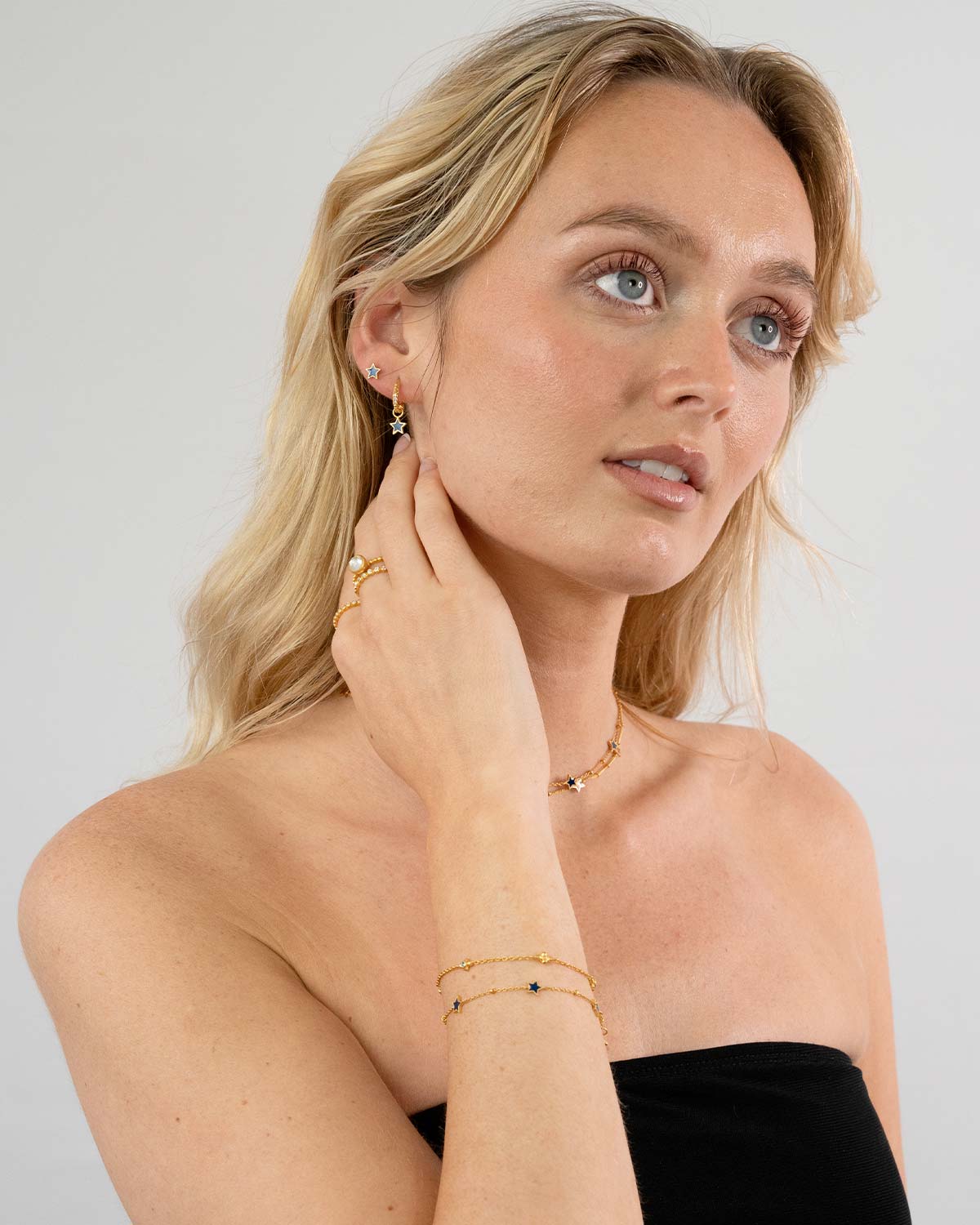 Model wearing gold mini hoop earrings with blue and orange enamel charms