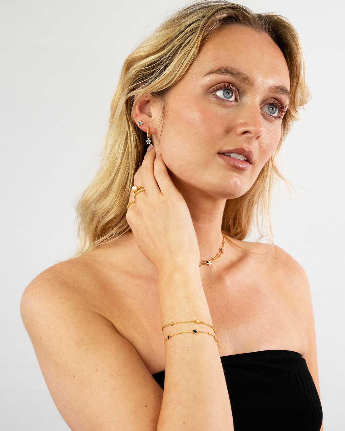 Model wearing a gold and silver adjustable bracelet with blue and orange enamel
